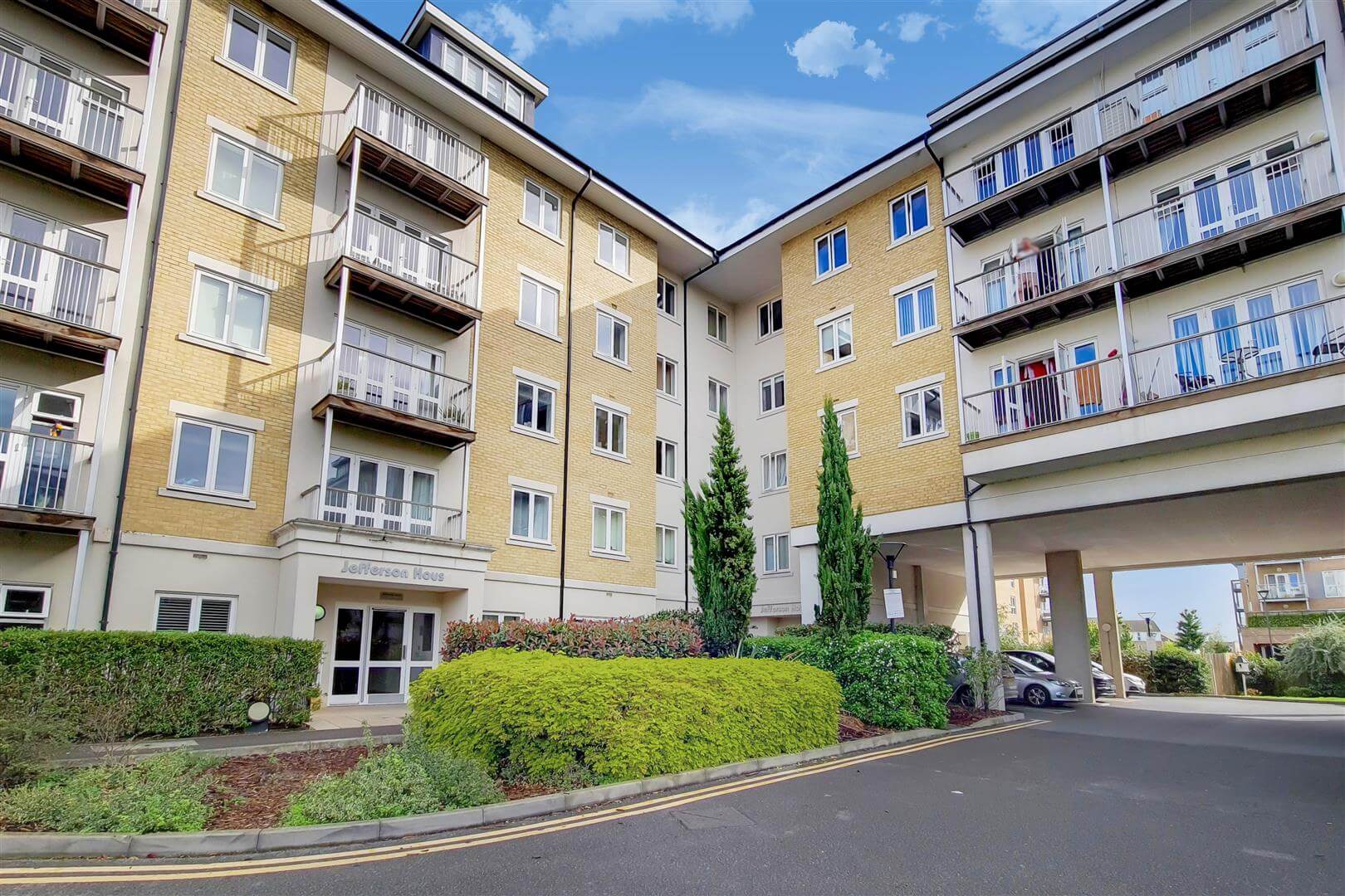 External view of a block of apartments, with shrubbery and resident parking area