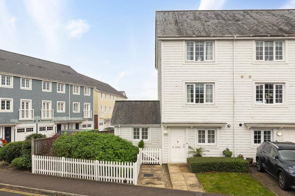 External view of a white cladded three-storey house with driveway, shrubbery and white picket fencing