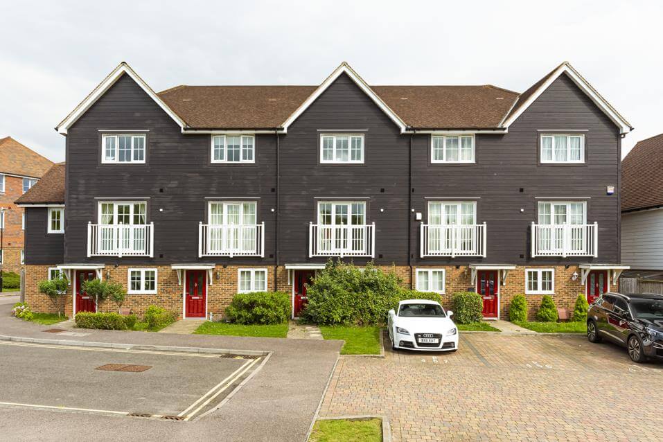 Row of five three-storey town houses, each with a dark red front door.