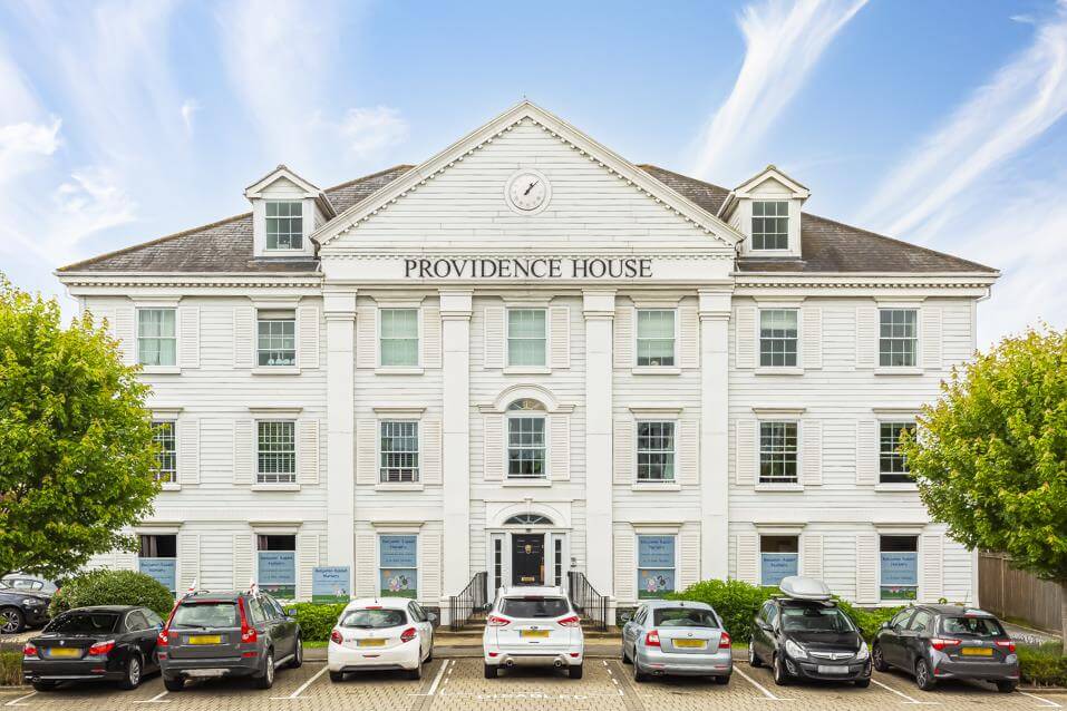 External view of a block of apartments with a row of parking bays to the front