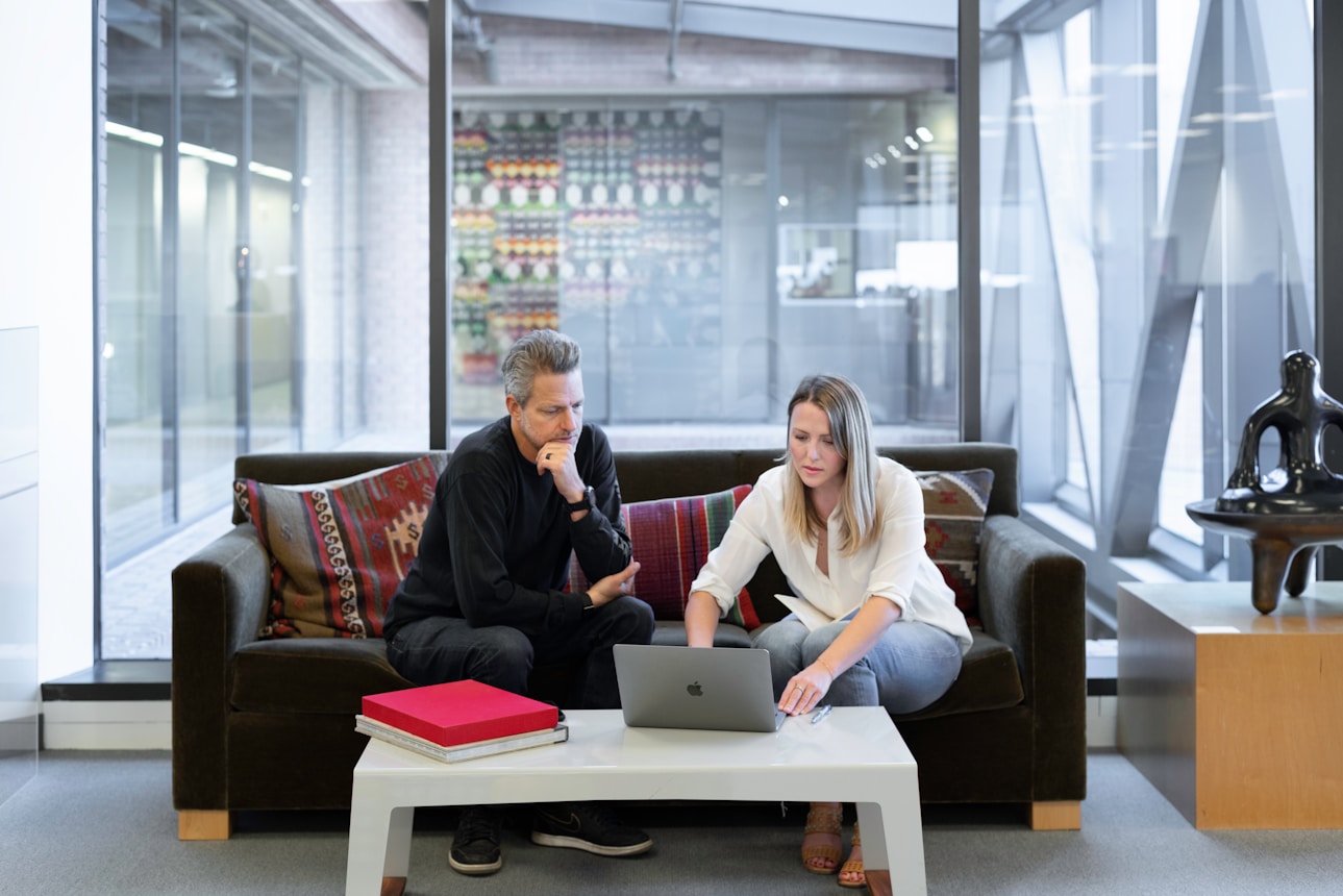 An employee shares project plans with a client whilst sat on a sofa