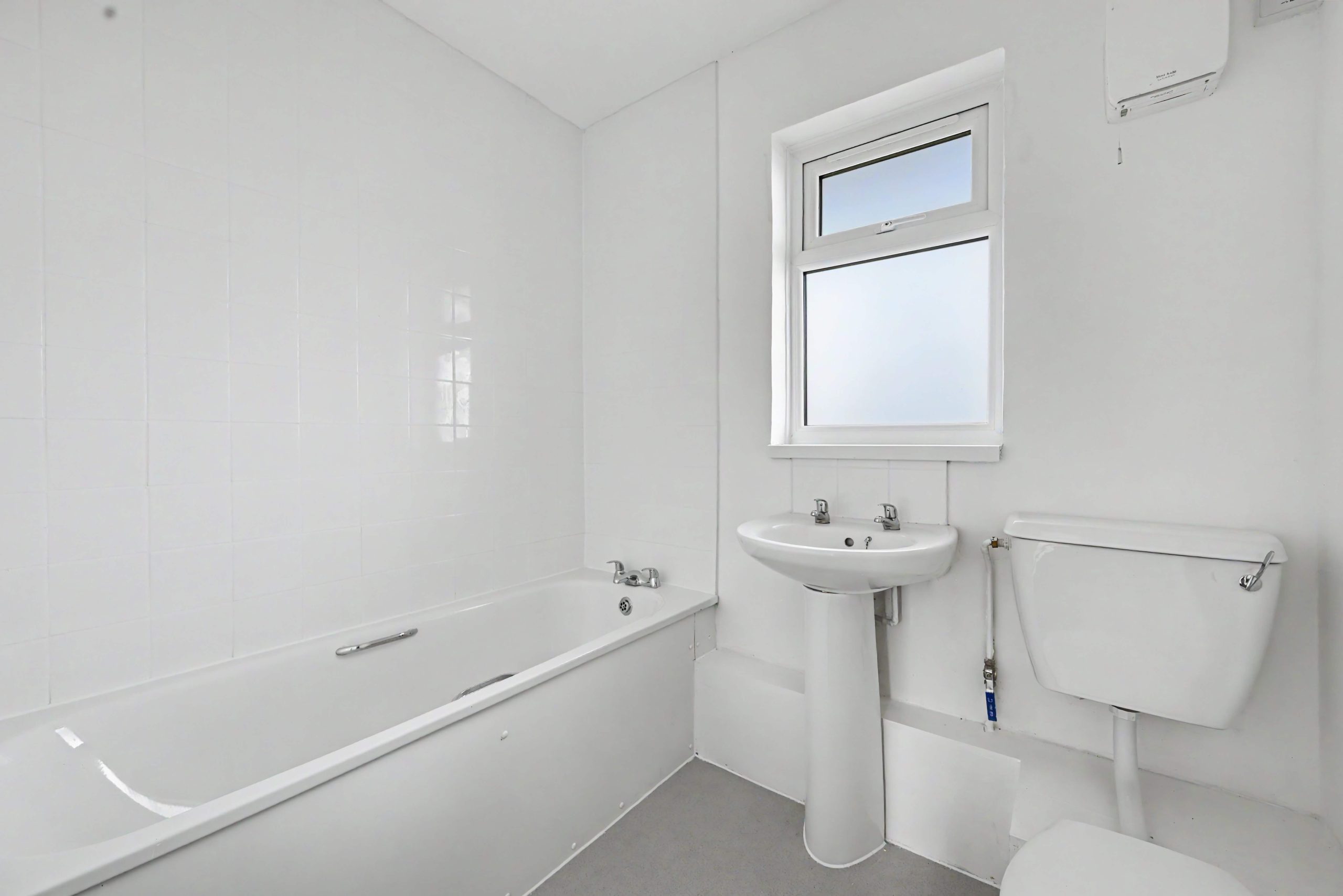 White 3 piece suite bathroom with white wall, white tiles and grey flooring