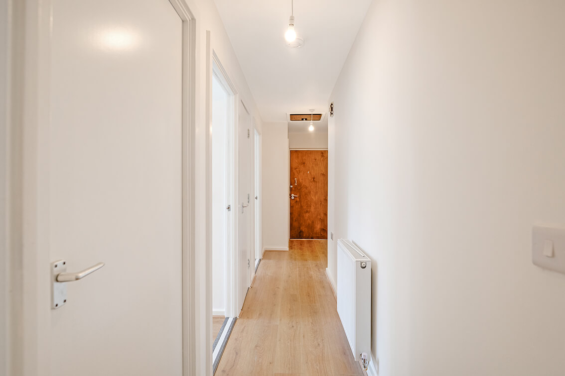 Refurbished hallway with white doors leading to other rooms, wooden flooring and a radiator. The front door can be seen at the end of the hallway