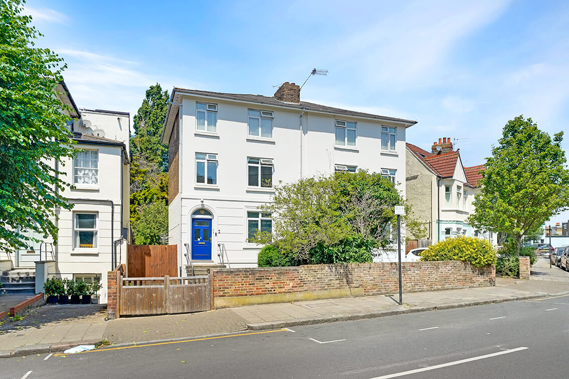 External view of a three storey terraced property on Allfarthing Road with a blue front door, perimeter wall and gated driveway.
