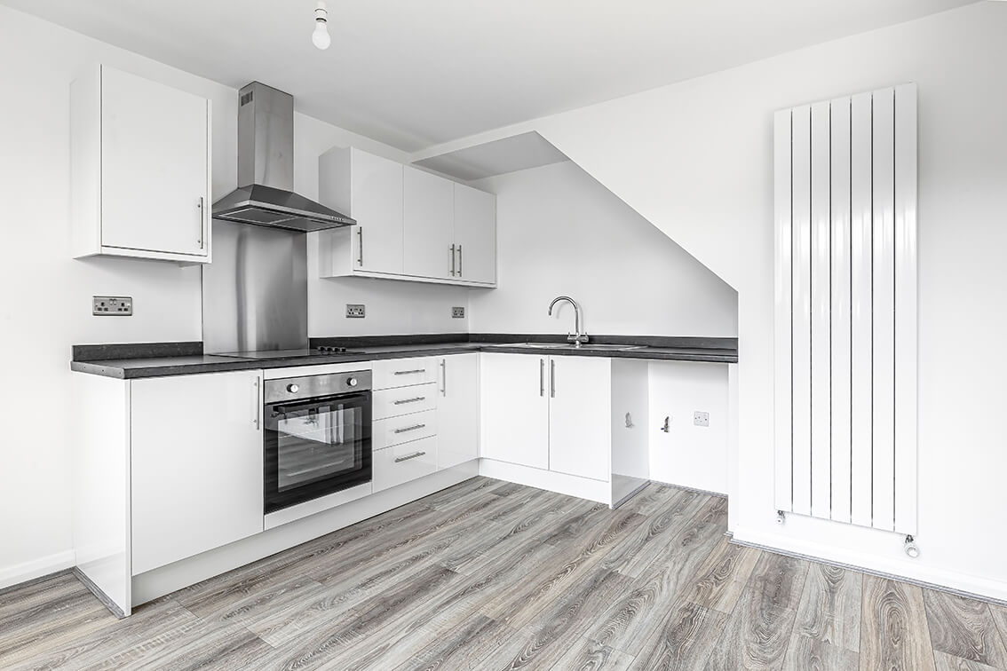 Refurbished kitchen with white kitchen units, white walls, oven with extractor hood and a modern white radiator and wooden flooring