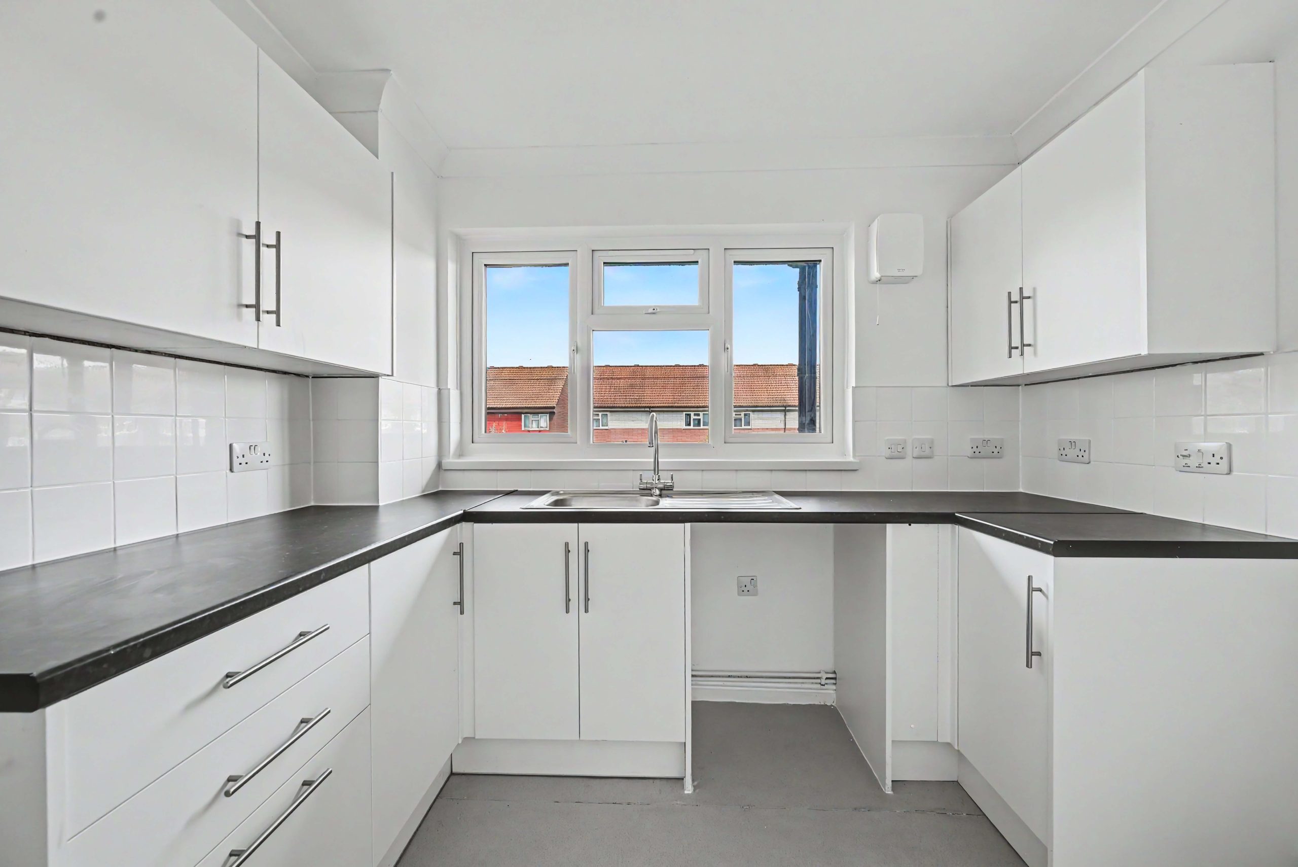 White kitchen with white kitchen cabinets, white walls, white tiles, a black worktop and a double glazed window