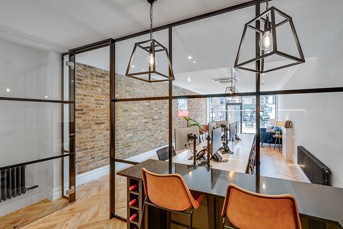 Internal view of a Madison Brook office overlooking a breakfast bar with two orange bar stools and two retro style ceiling lights