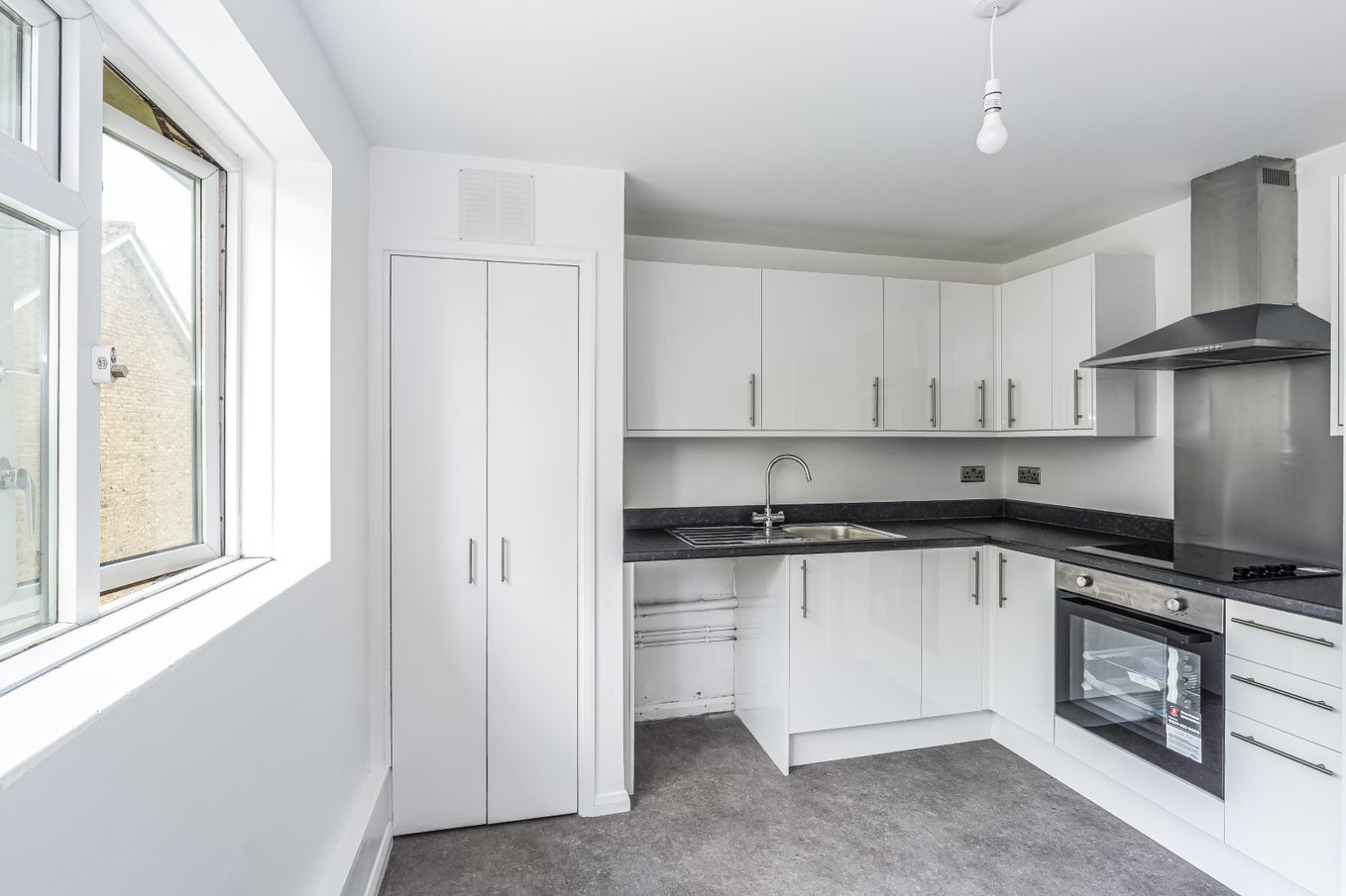 Refurbished kitchen with white units, oven and extractor hood, sink and space for a dishwasher. there is also an integrated storage cupboard
