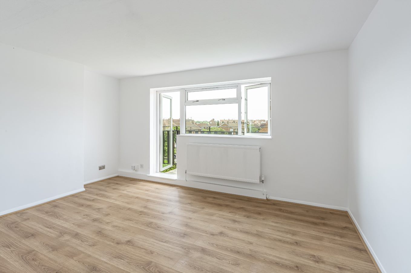Refurbished reception room, with white walls, radiator, wooden flooring, double glazed windows and door which provides balcony access