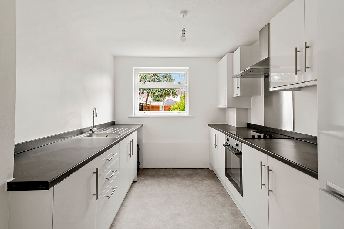 Refurbished kitchen with white walls, grey floor, white kitchen units with a black worktop. There is a sink, oven and hob with extractor hood.