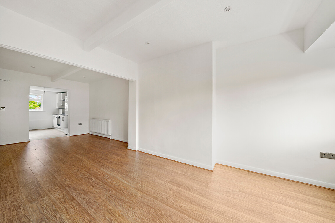 Refurbished open plan living area with white walls, inset ceiling lights, wooden flooring and a radiator.