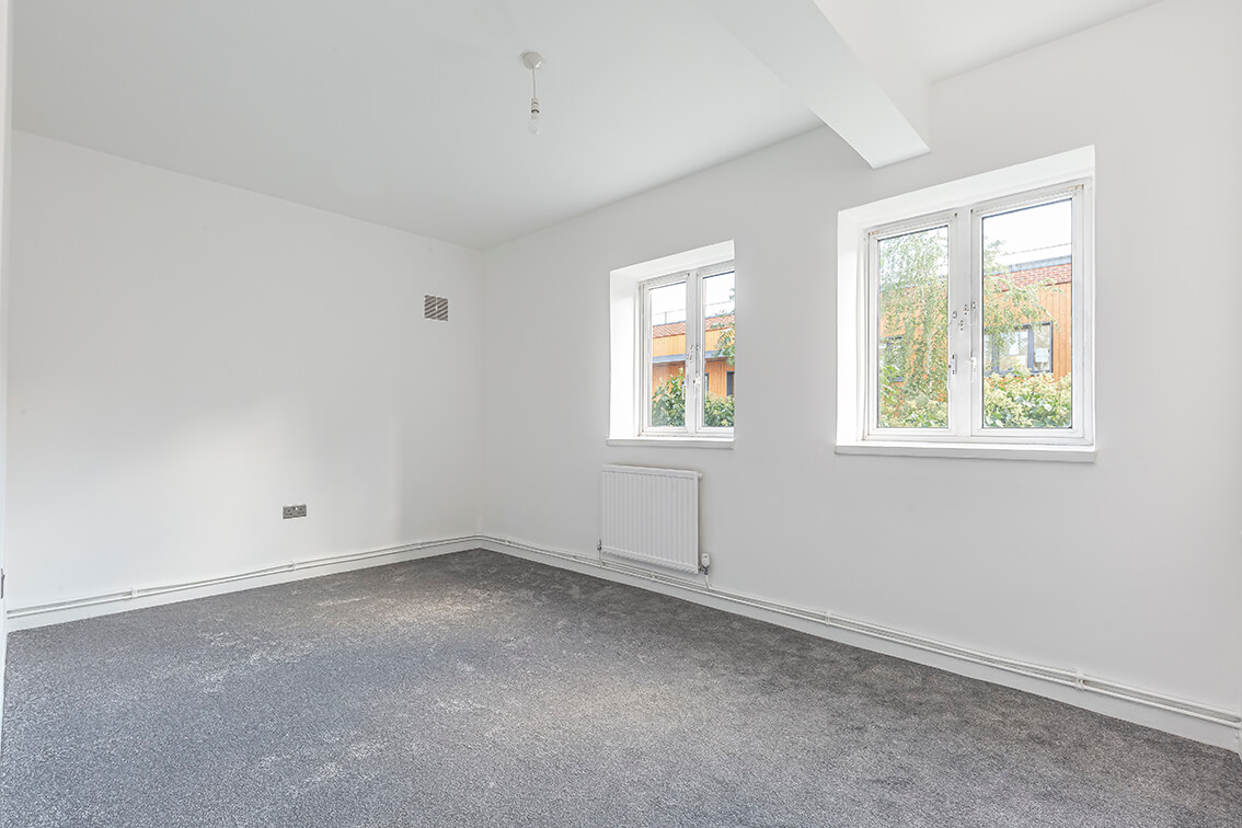 Refurbished room with white walls, grey carpet, two double glazed windows and a radiator
