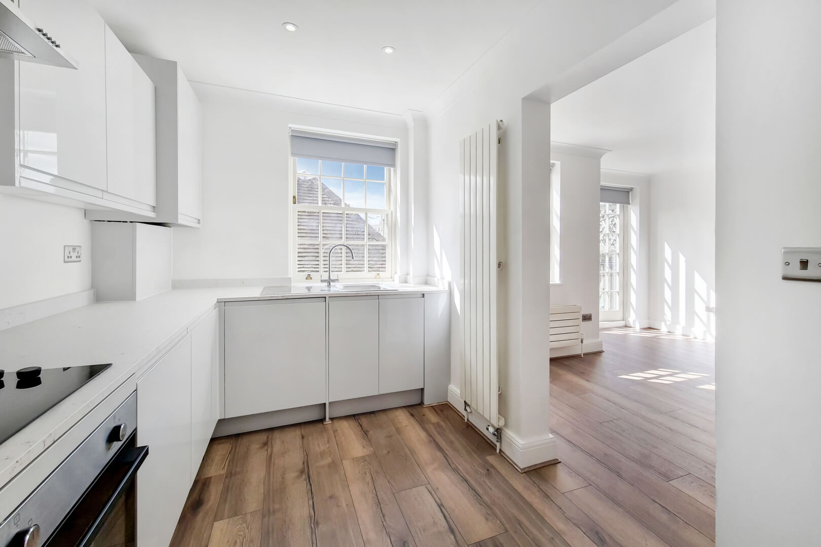 Modern white kitchen with wooden flooring and a modern white radiator leading through to an open plan living space